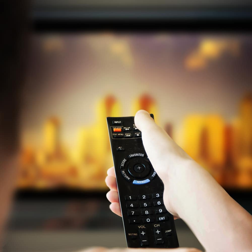 Main avec télécommande devant un écran de télévision