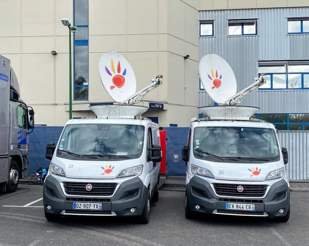 Deux camions Ad Valem avec paraboles sur le toit garés devant un bâtiment