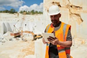 Homme d'âge moyen avec une tablette regardant des instruction en ligne en se tenant sur un terrain de construction