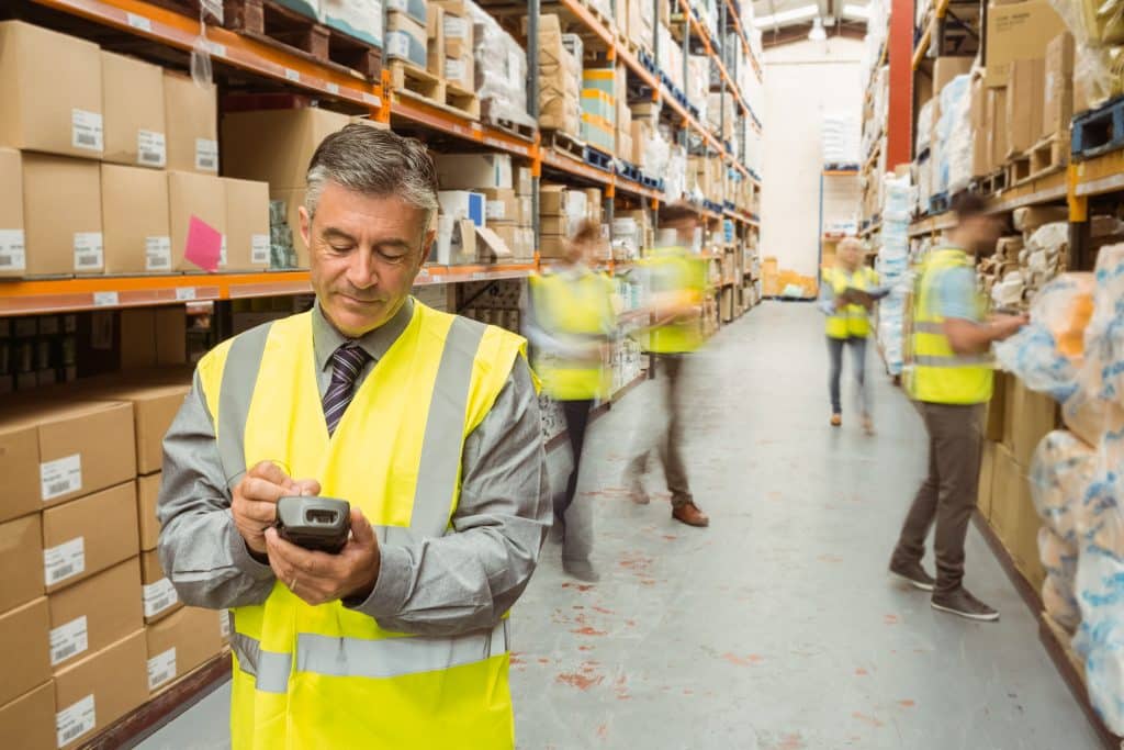 smiling,male,manager,using,handheld,in,a,large,warehouse